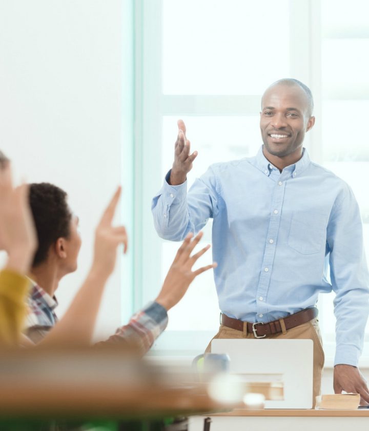 teacher in front of classroom choosing a student with raised hand to answer question